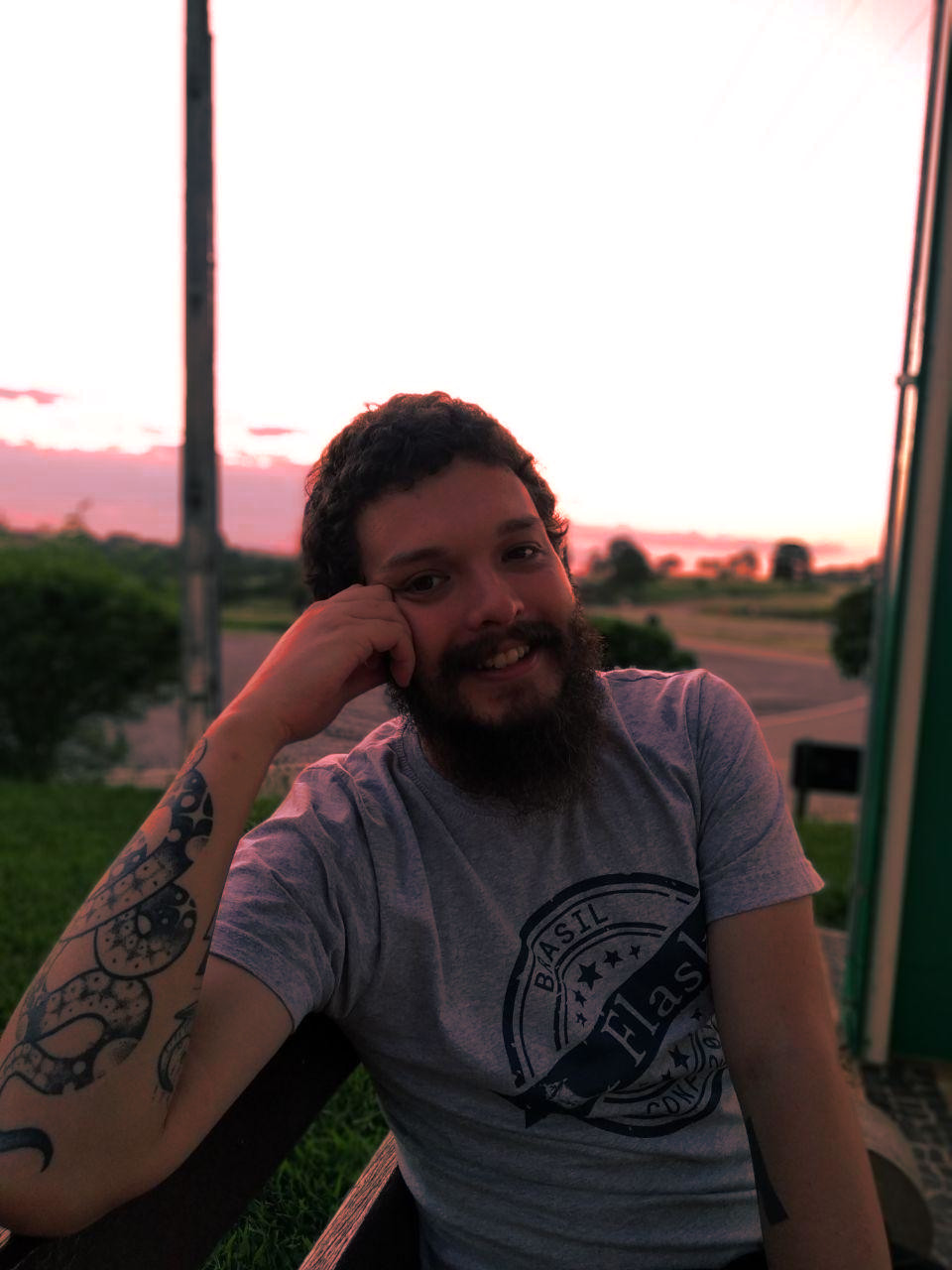 Uma fotografia minha, Dunossauro, sentado em um banco com um por do sol ao fundo